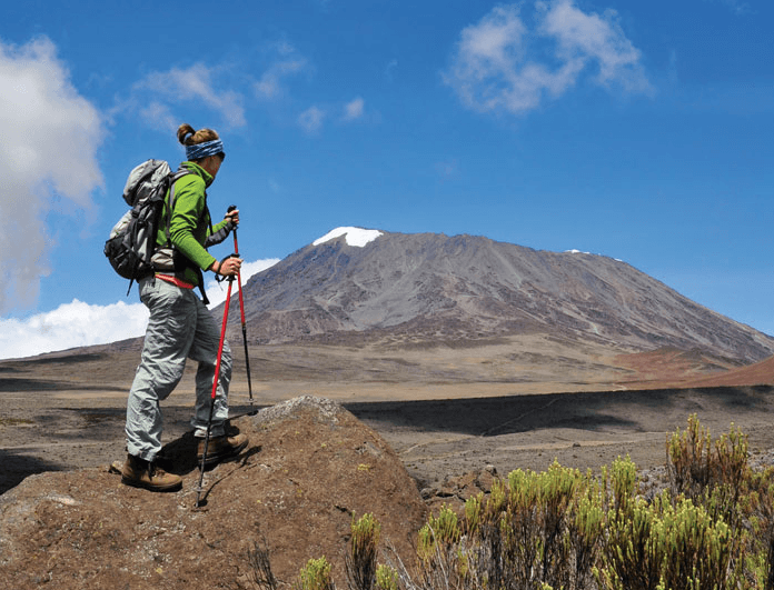 Bergsteigerin steht auf Felsen und genießt Aussicht auf den Kilimandscharo