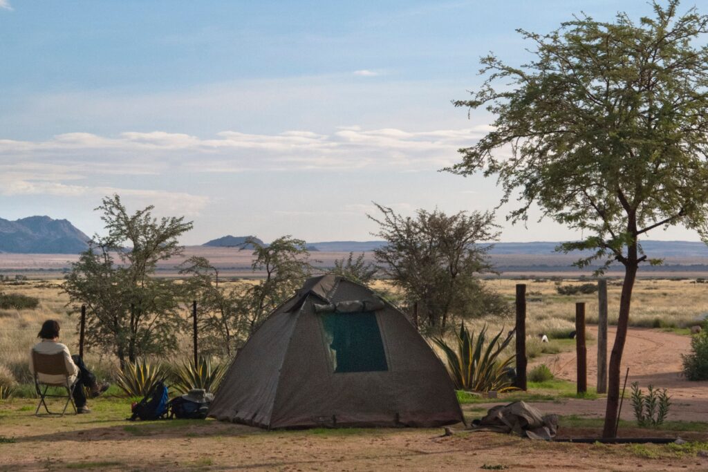 Frau sitzt auf einem Klappstuhl neben einem Kuppelzelt in der afrikanischen Natur