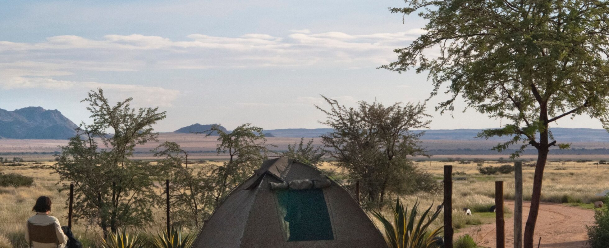 Frau sitzt auf einem Stuhl neben einem Kuppelzelt in der afrikanischen Natur