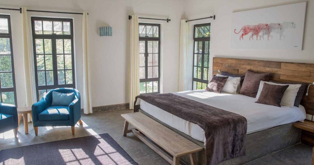 Arusha Villa Zimmer mit Bett, türkisen Sesseln und großen Fenstern