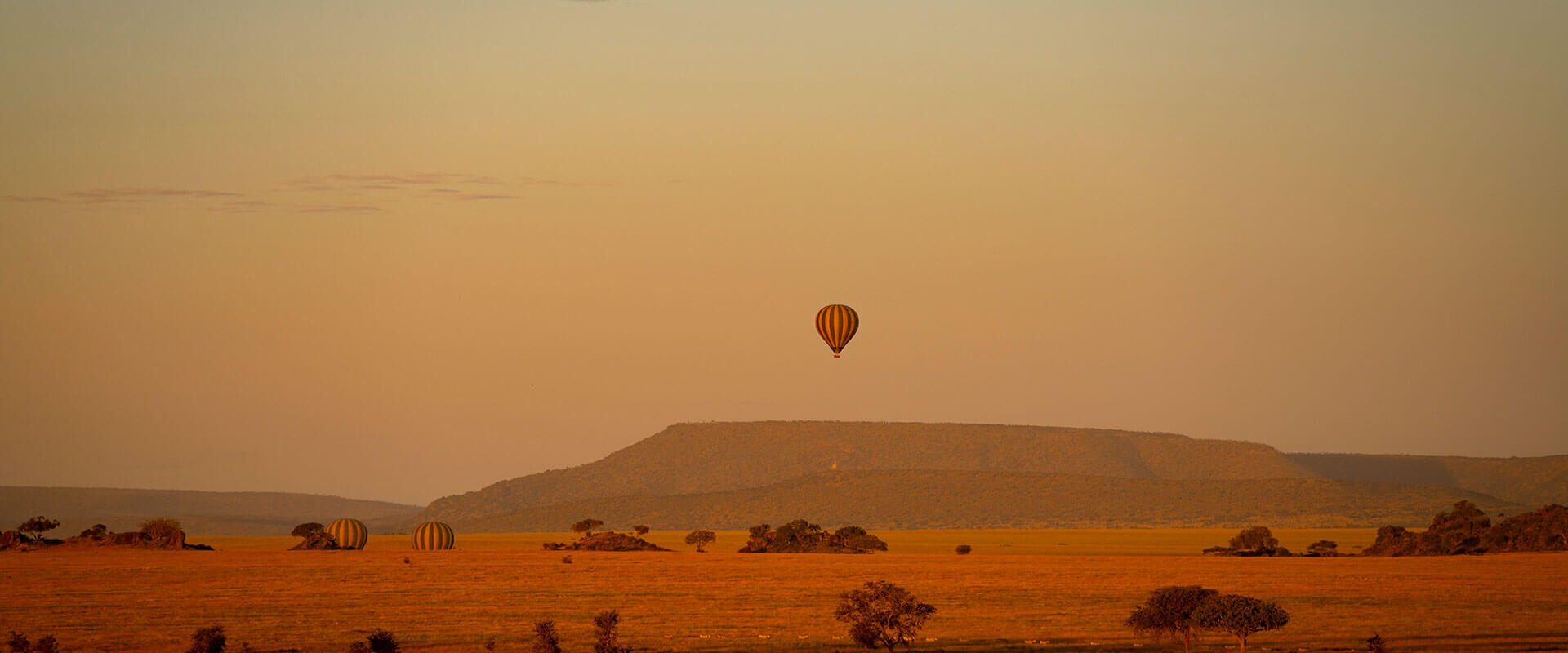 Heißluftballon in der Ferne über Landschaft und Berg bei Sonnenuntergang