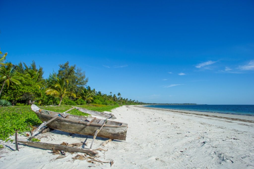 Sandstrand mit altem Holzboot neben grüner Wiese