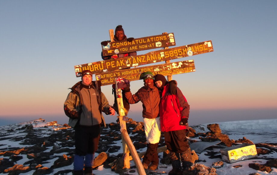 Drei Wanderer stehen vor Schild auf dem Gipfel des Kilimandscharo