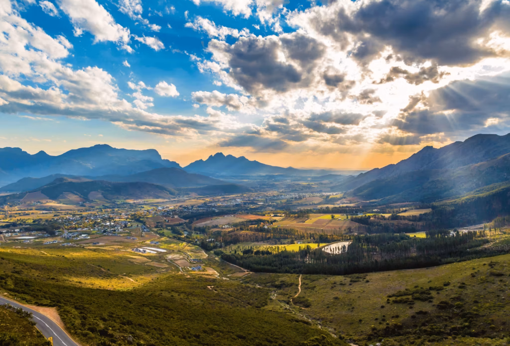 The landscape of Franshhoek in South Africa from above, with mountains in the background and the sun shining through darker clouds